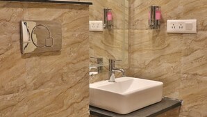 A modern bathroom with a marble wall, a white toilet, a sink with a mirror above it, and a showerhead. - Shiv Shakti Hostel (Rishikesh)