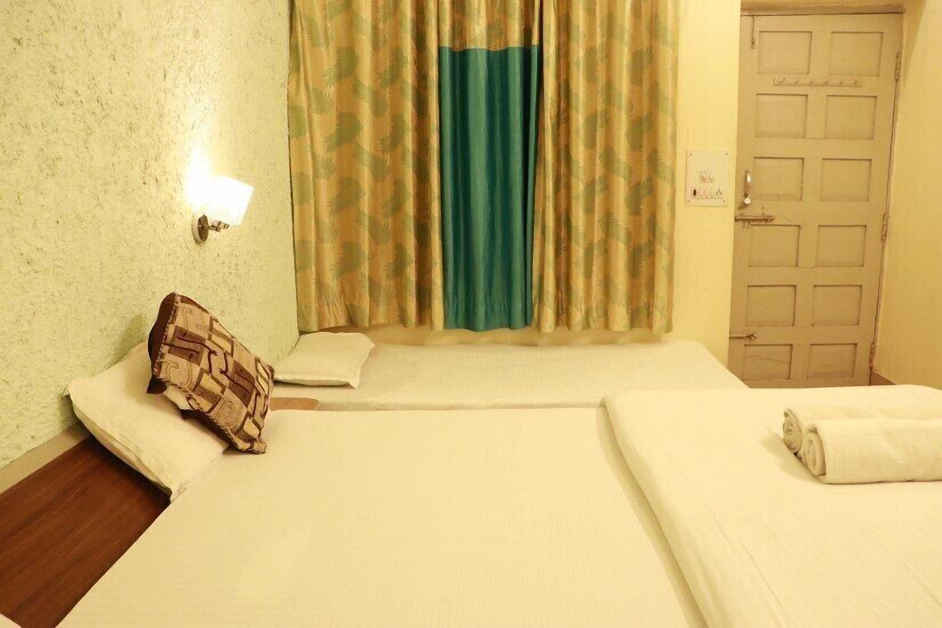 A hotel room with a bed, a pillow, a wall-mounted light, and a door.