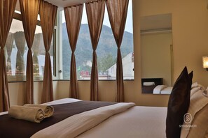 Ett hotellrum med en säng, gardiner, ett fönster med utsikt över bergen och en spegel.