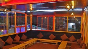 A cozy seating area with cushioned benches and sofas, large windows offering a view, and ambient lighting. - Shiv Shakti Hostel (Rishikesh)