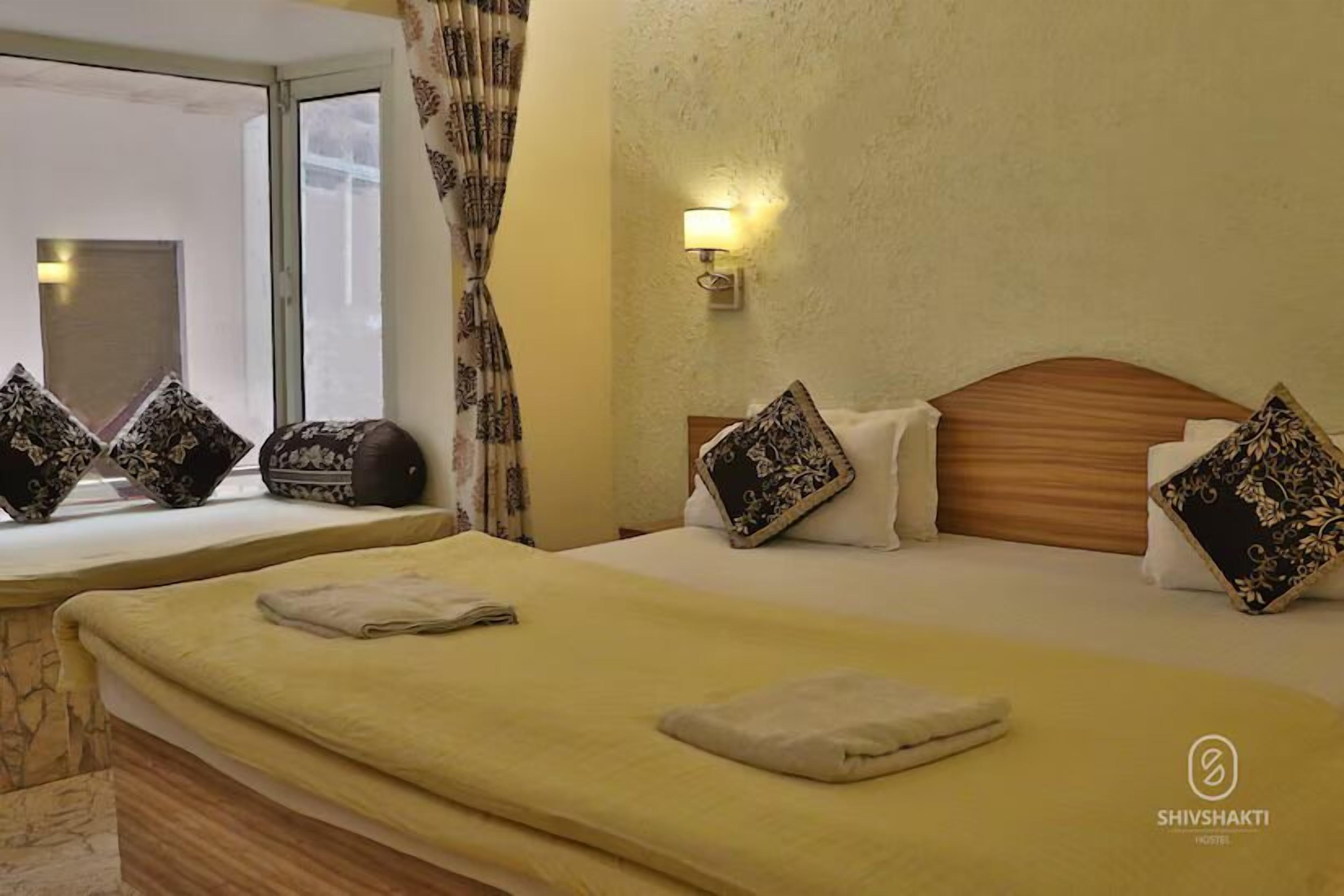 A hotel room with two beds, each with a headboard, pillows, and a bedside lamp.