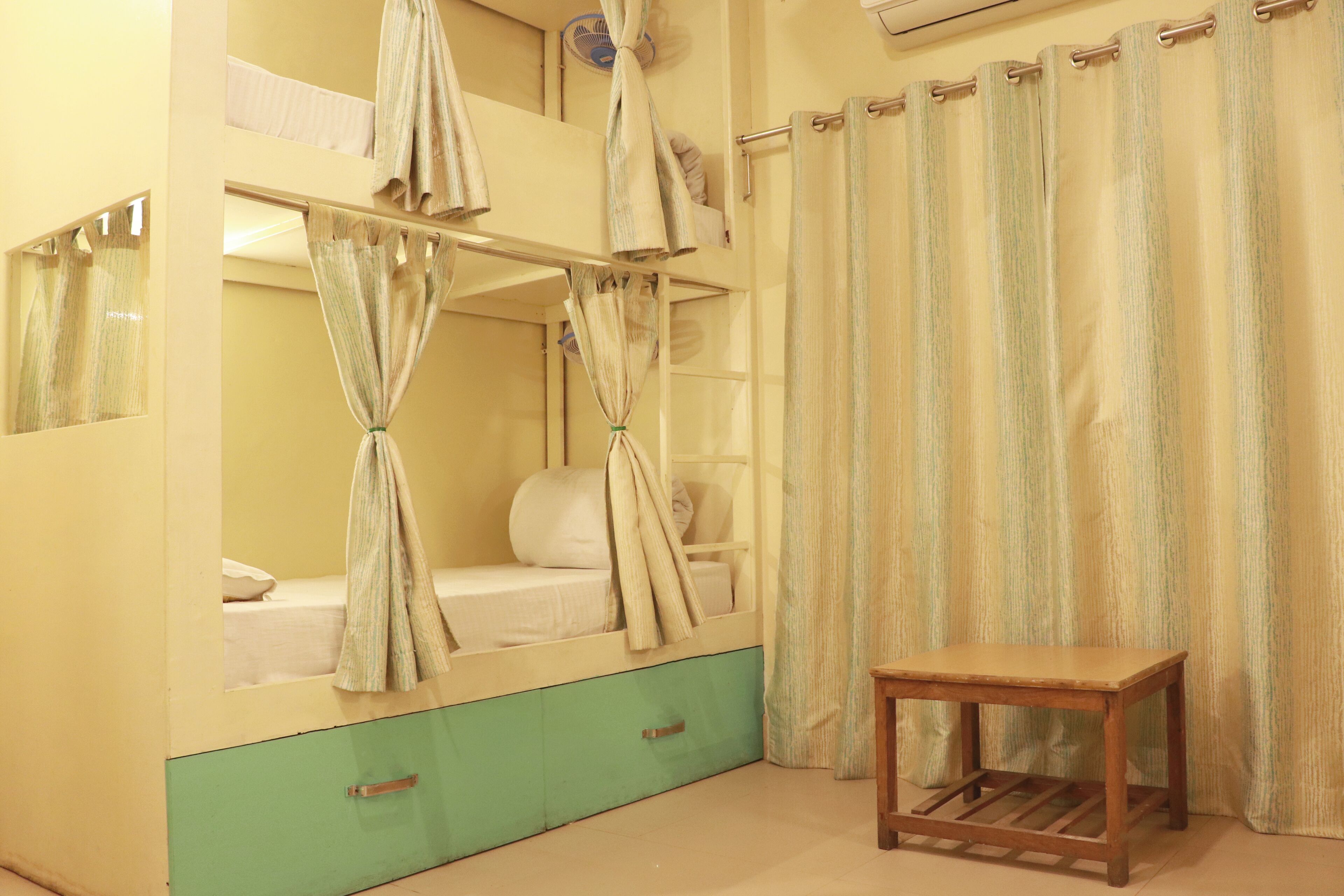Une chambre avec un lit superposé, une commode verte, une table en bois et un rideau à rayures.