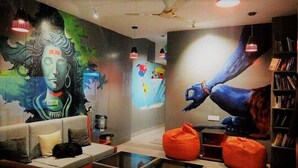 A modern lounge with a mural, a sofa, a coffee table, and a bookshelf. - Shiv Shakti Hostel (Rishikesh)