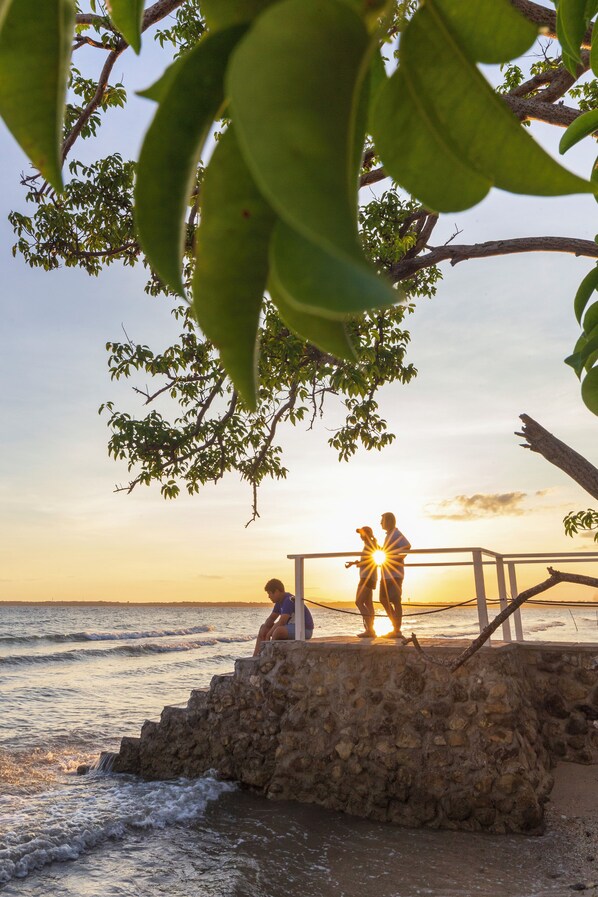 A stone staircase leading to a beach with a couple standing at the top, overlooking the ocean at sunset.