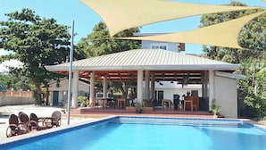 A swimming pool with a covered seating area and outdoor furniture.