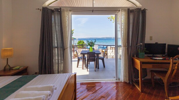 A hotel room with a bed, a desk with a computer, and a view of the sea through an open door.