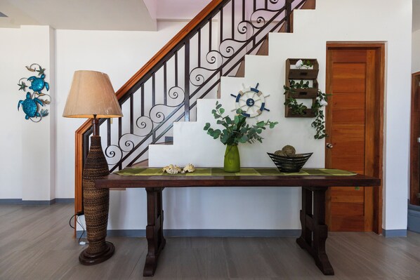A wooden table with a lamp and decorative items, a staircase with a railing, and a door with a plant on the wall. - 5-Bedroom Beachfront Mansion in Calatagan with Outdoor Pool (Calatagan)