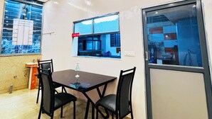 A dining area with a table and chairs, a window with a view of the outside, and a kitchen visible through the window.
