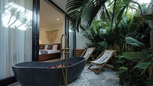 Un área de spa con una bañera negra grande, una silla de madera y una cama con vistas a la habitación.