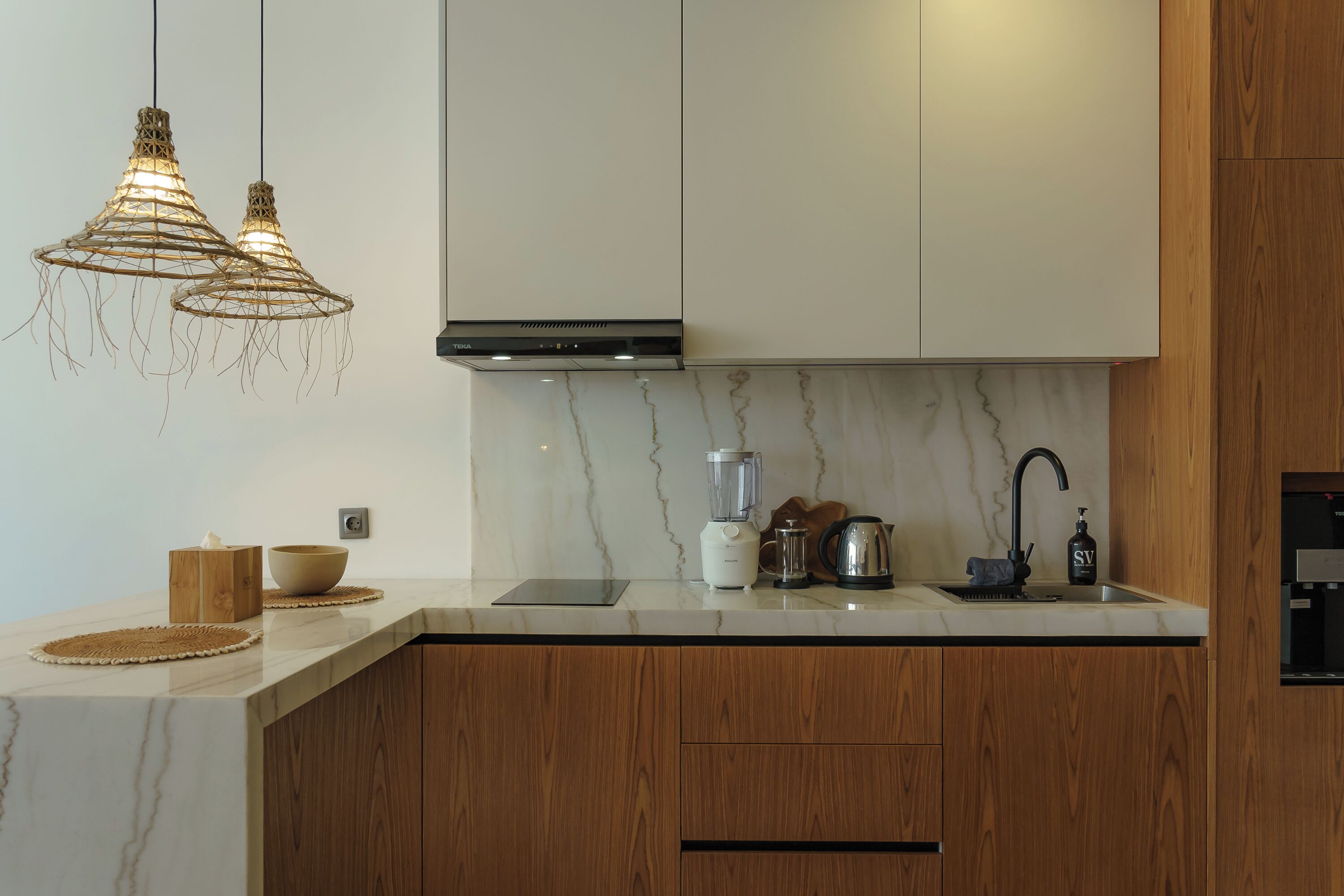 Una cucina moderna con mobili in legno, un piano di lavoro in marmo, un piano cottura integrato e lampade a sospensione.