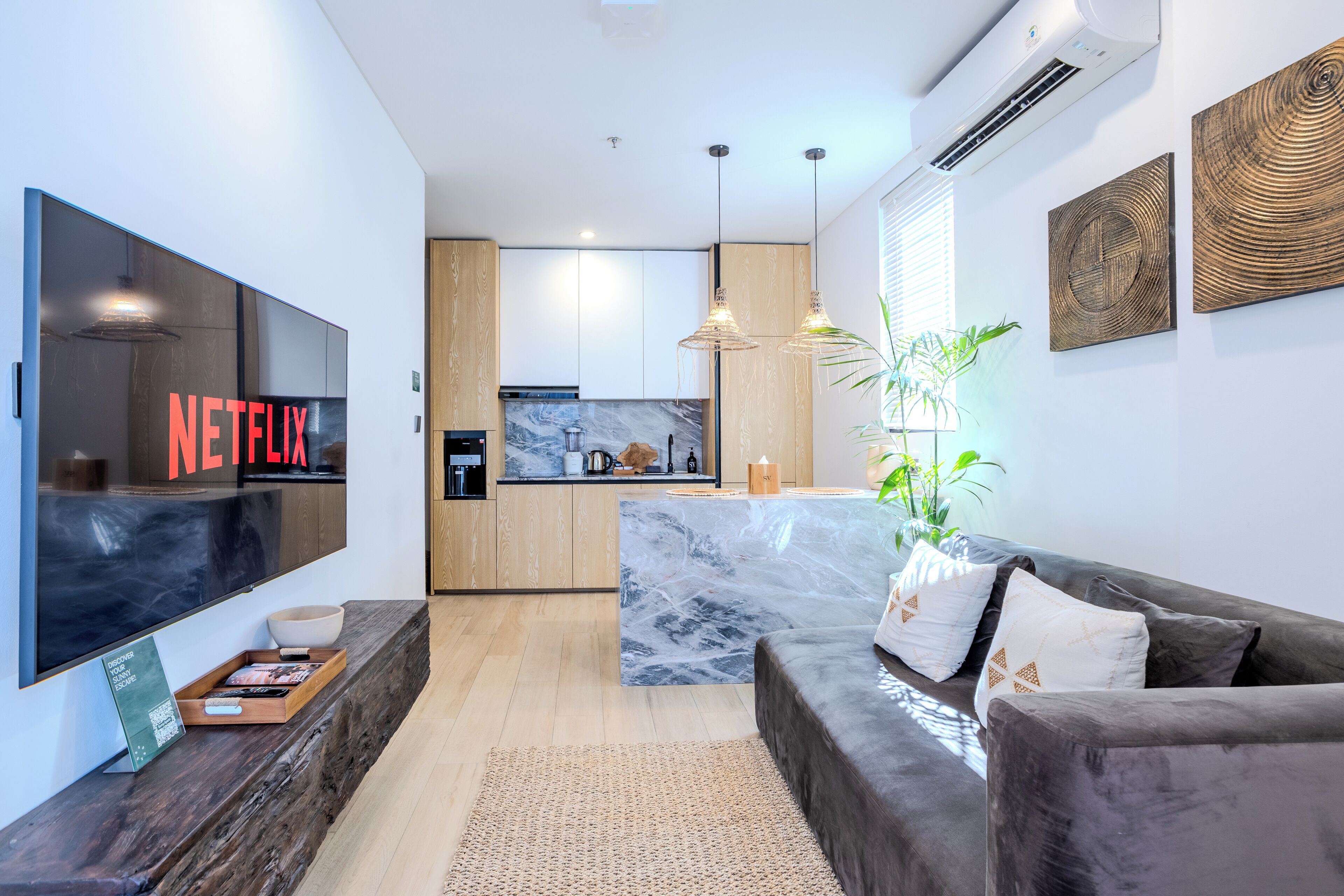 A modern living room with a large flat-screen TV, a dark-colored sofa, and a marble accent wall.