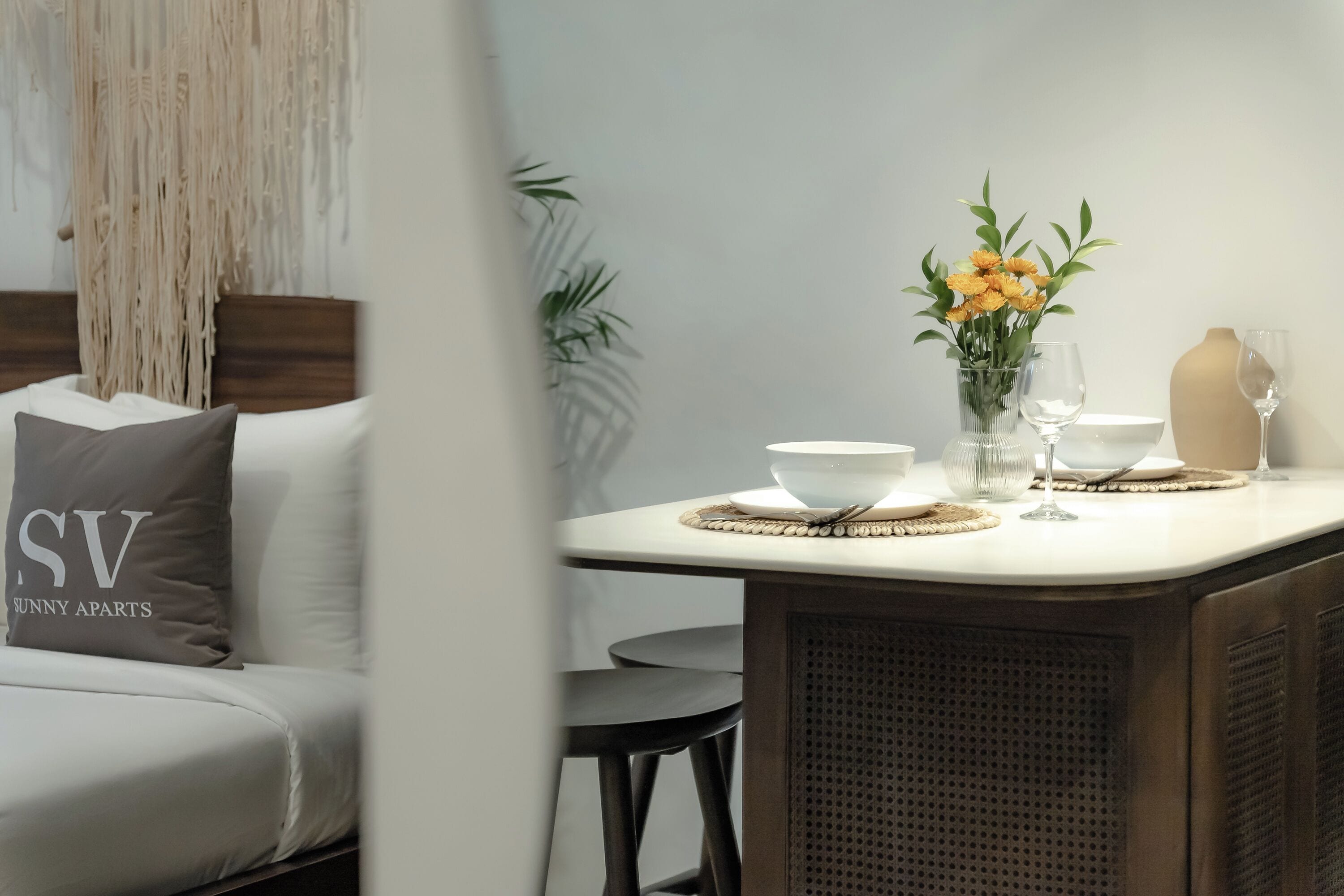 A modern living room with a sofa, a dining table with a vase of flowers, and a bar area.