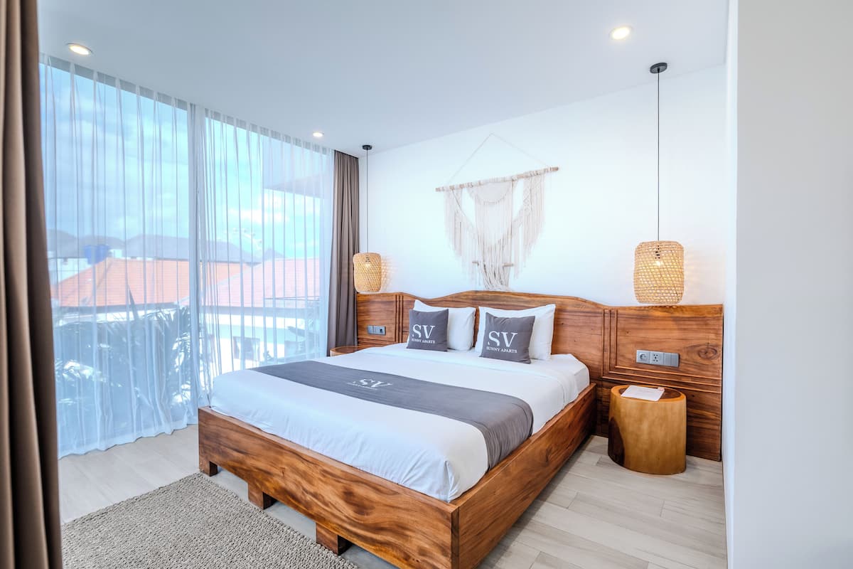 A modern bedroom with a wooden bed, white bedding, and a view of the outdoors.