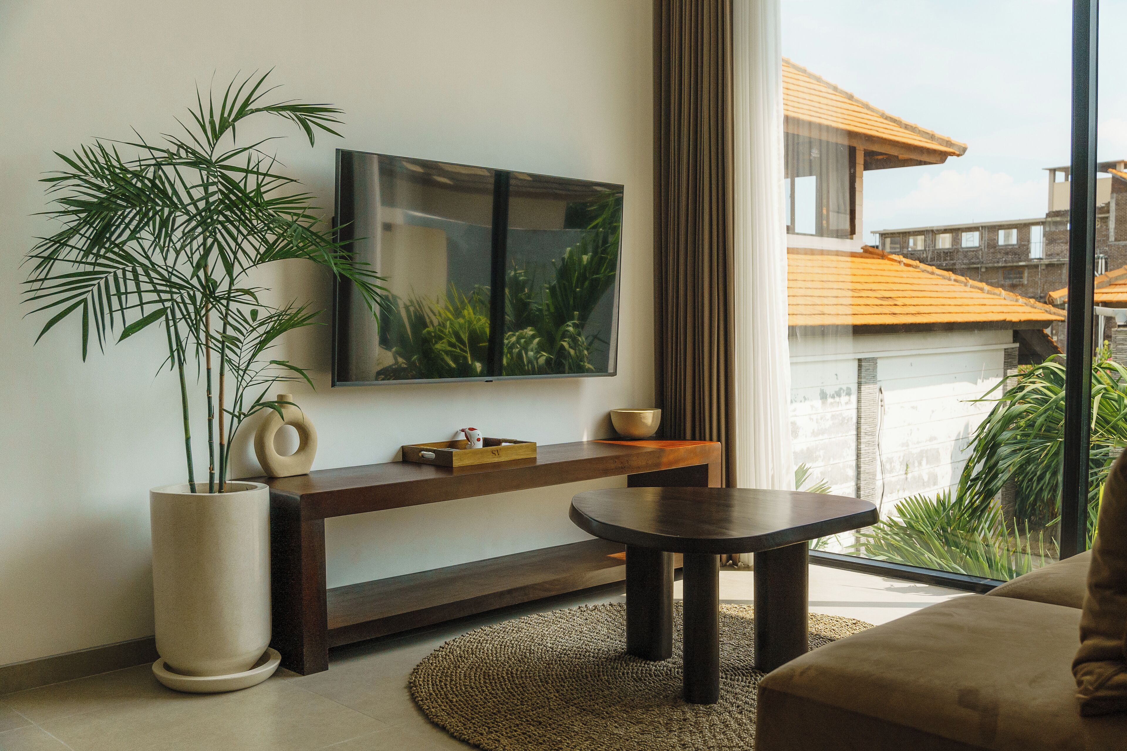 Una sala de estar moderna con un televisor grande, una planta en maceta, un mueble bajo de madera y una mesa de centro redonda.