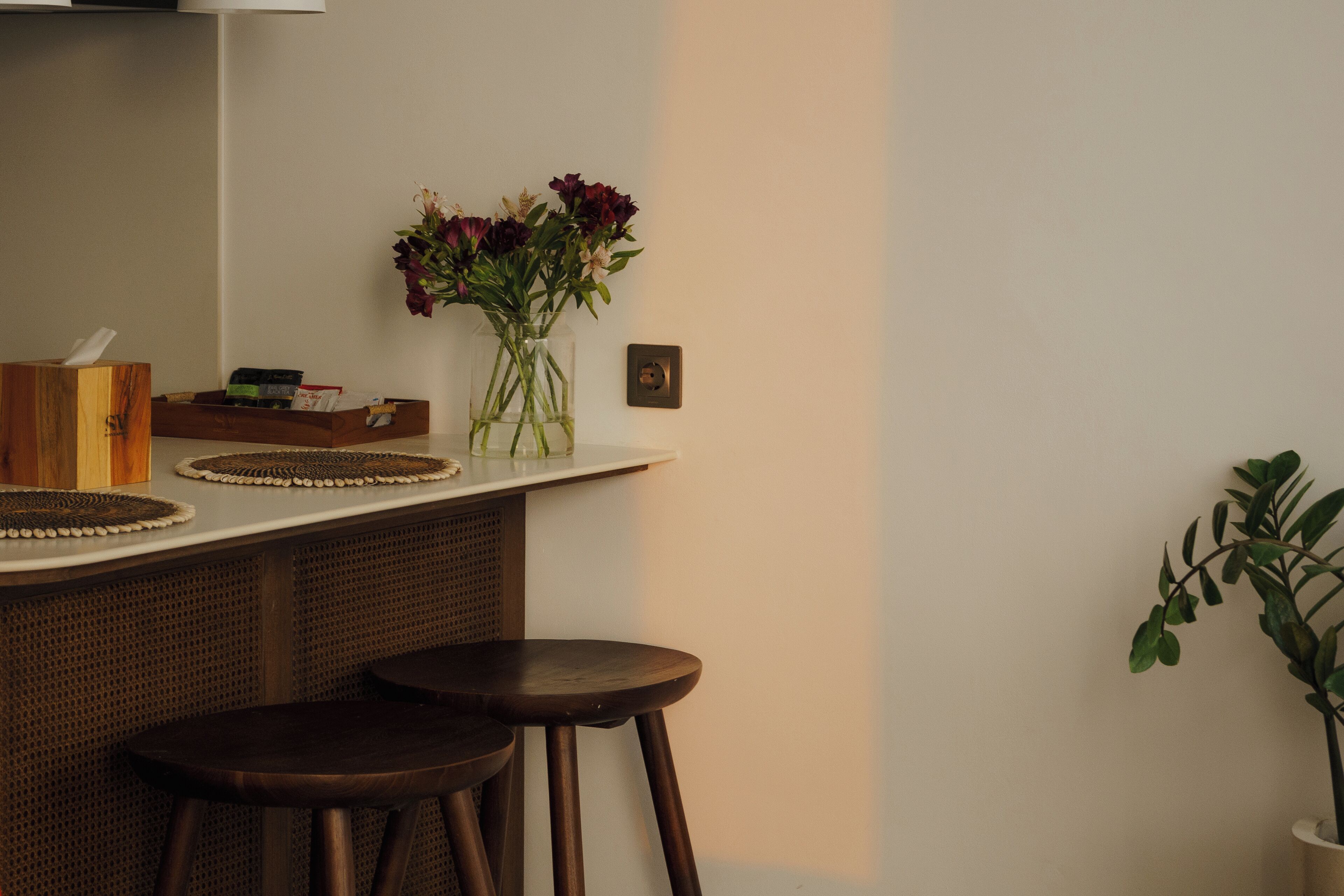 A kitchen counter with a vase of flowers, two stools, and a potted plant.