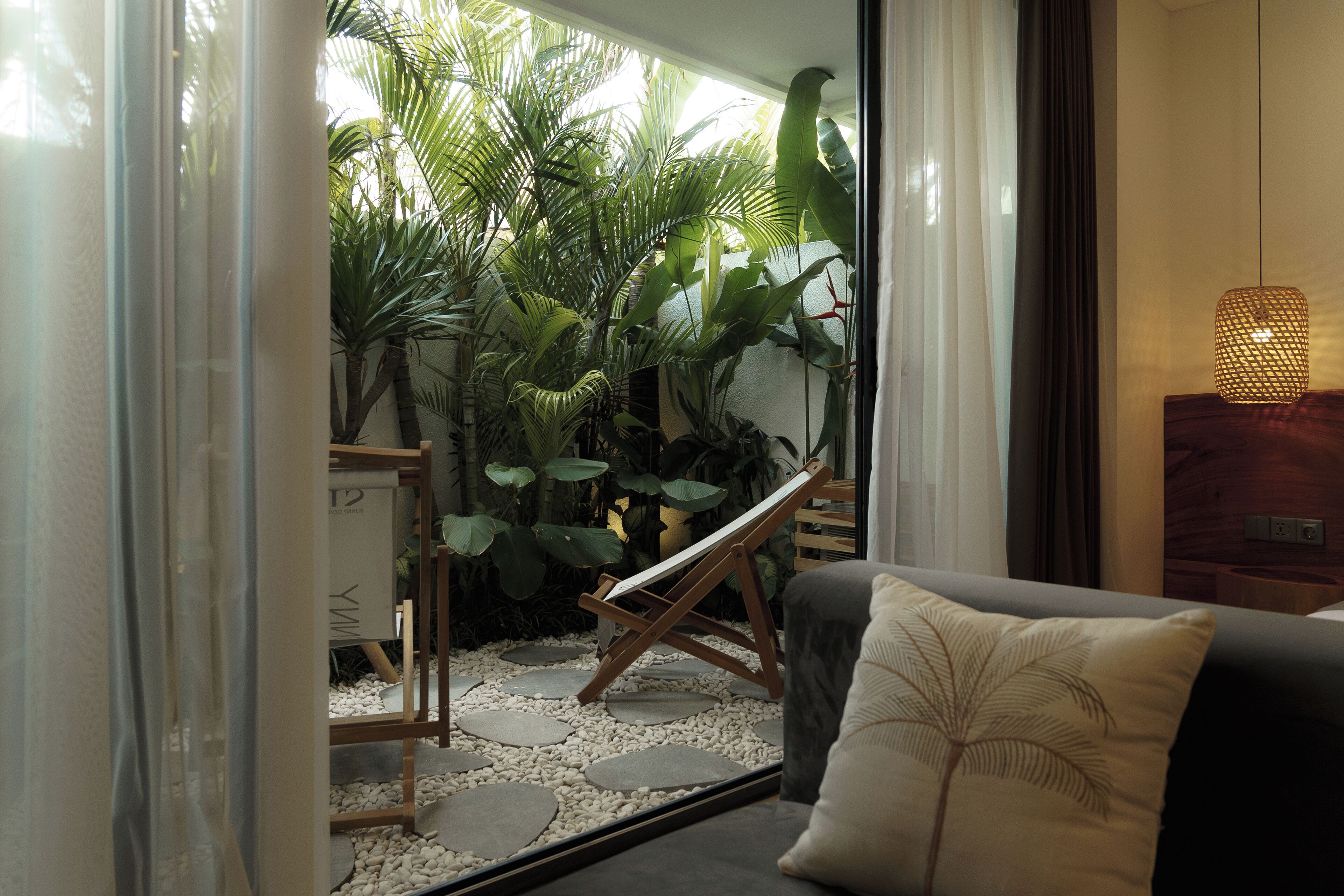 Ein Zimmer mit einem Bett, einem kleinen Tisch und Blick auf einen Garten mit Pflanzen und einer hölzernen Bank.