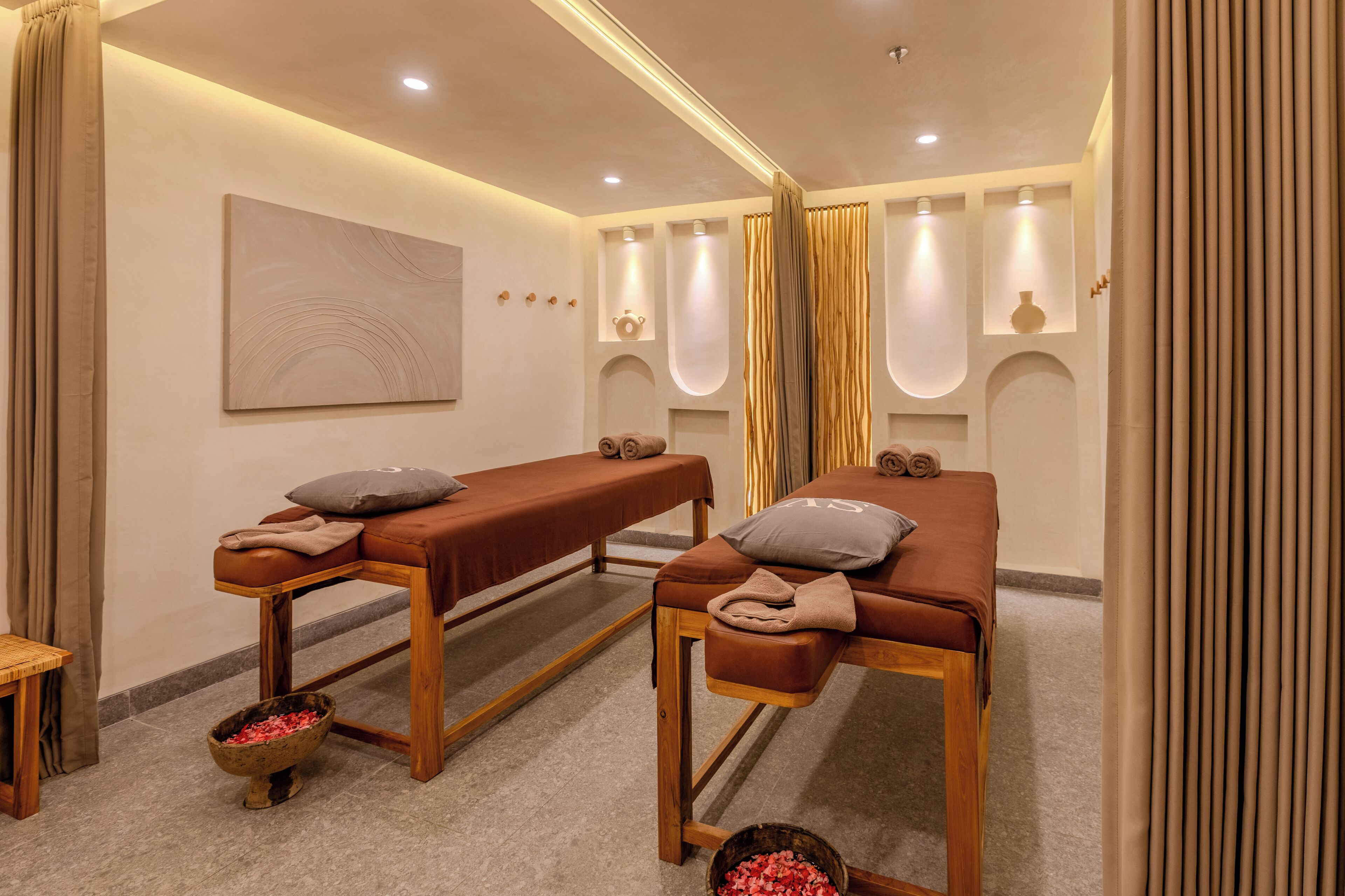Ett spa-rum med två massagebänkar, ett trägolv, ett konstverk som hänger på väggen och en liten träpall.