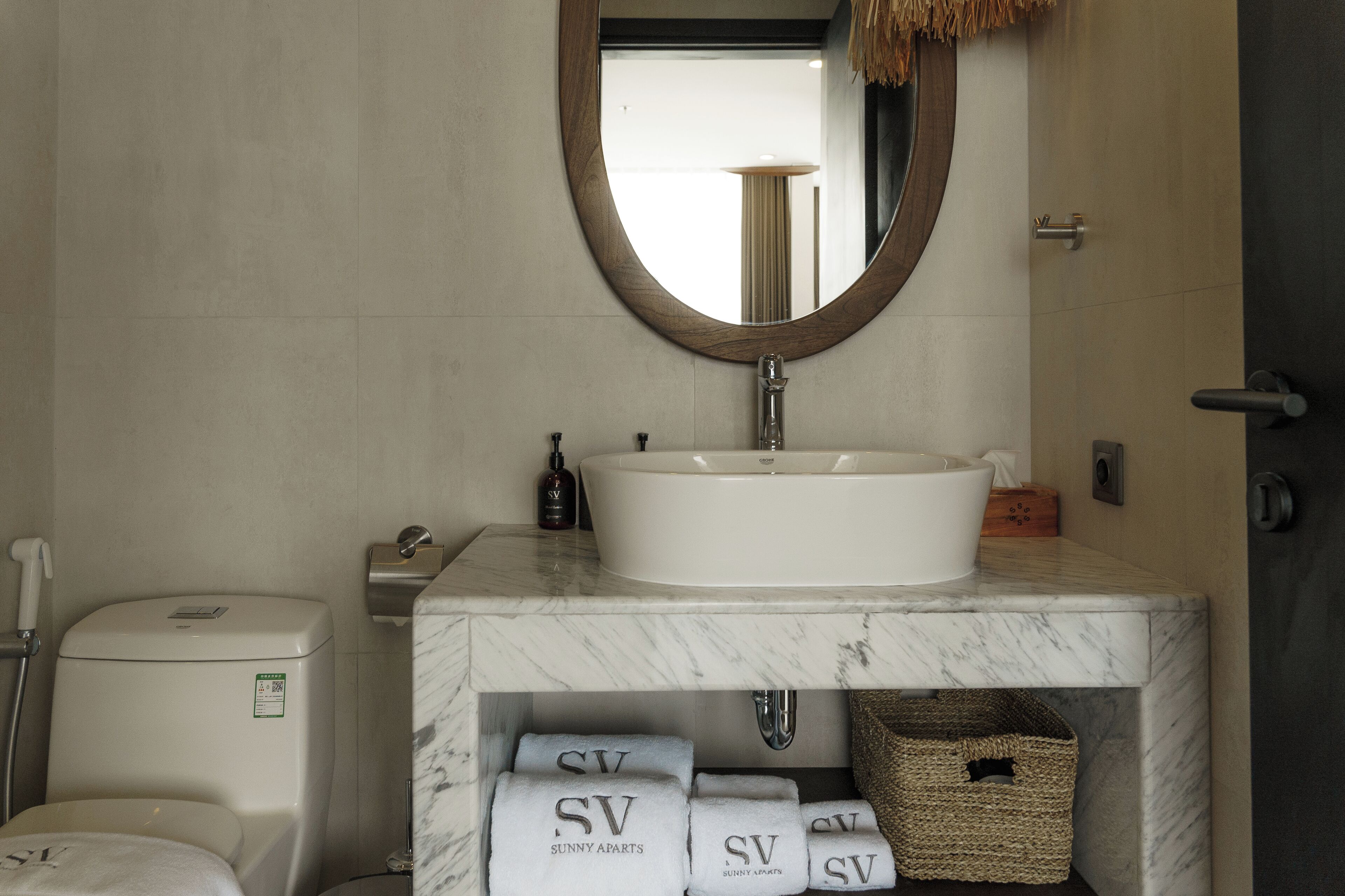 A bathroom with a white sink, a mirror, and a toilet. There are towels and a basket under the sink.