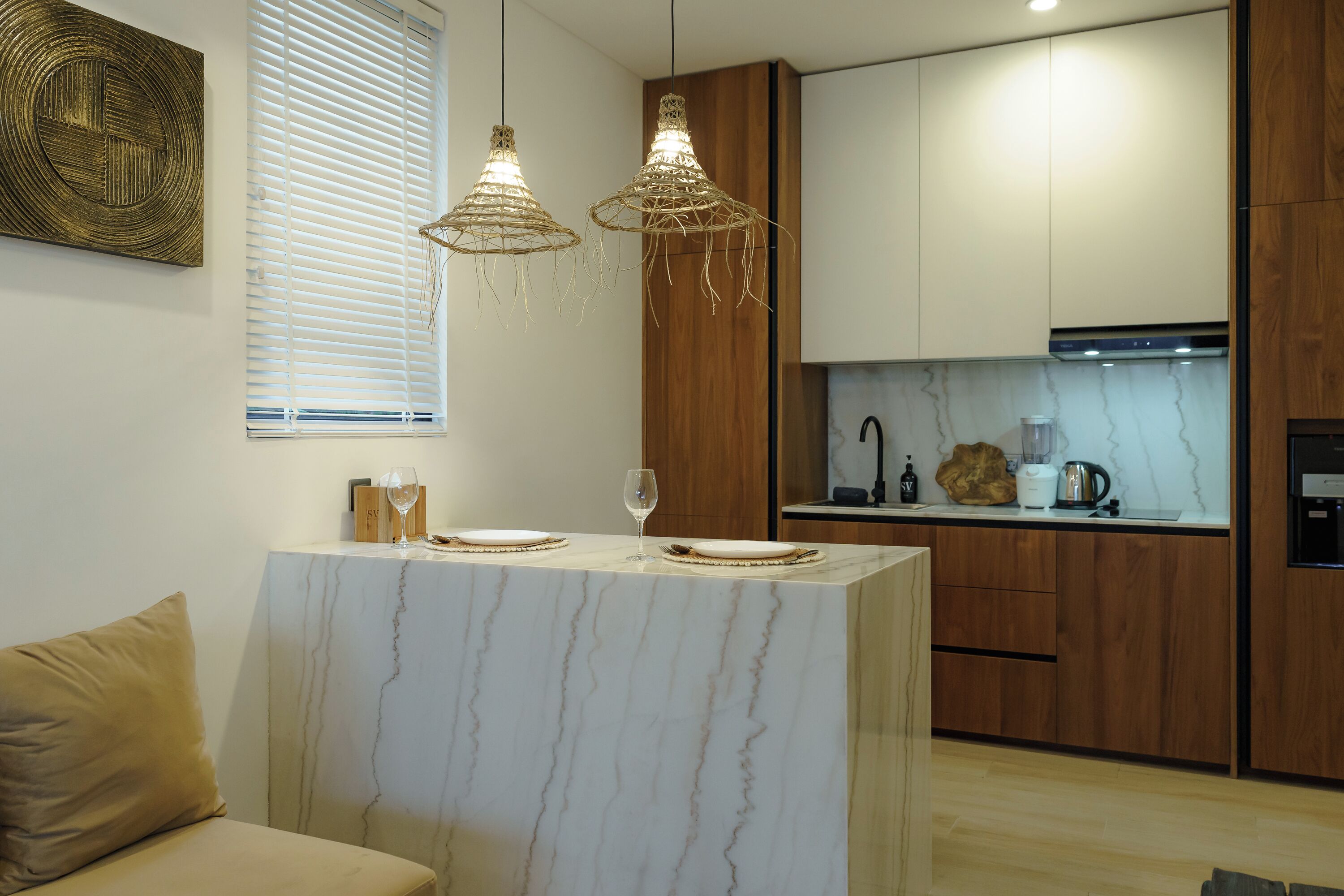 Una cocina moderna con una isla de mármol, armarios de madera y luces colgantes.