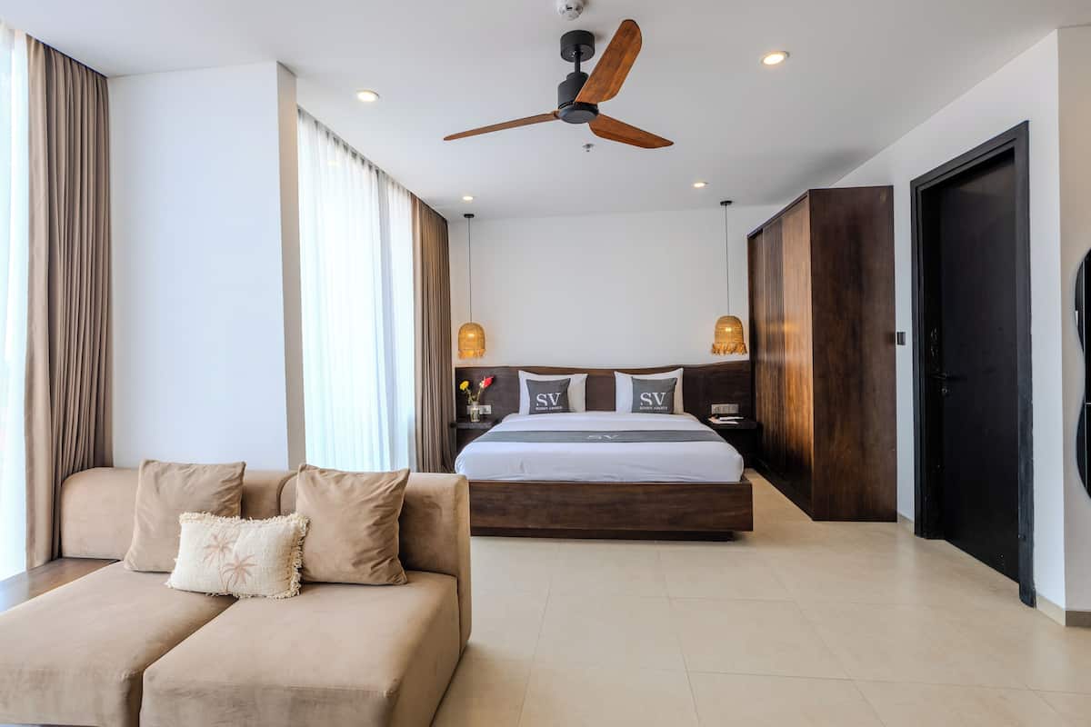 A modern hotel room with a large bed, a sofa, and a ceiling fan.