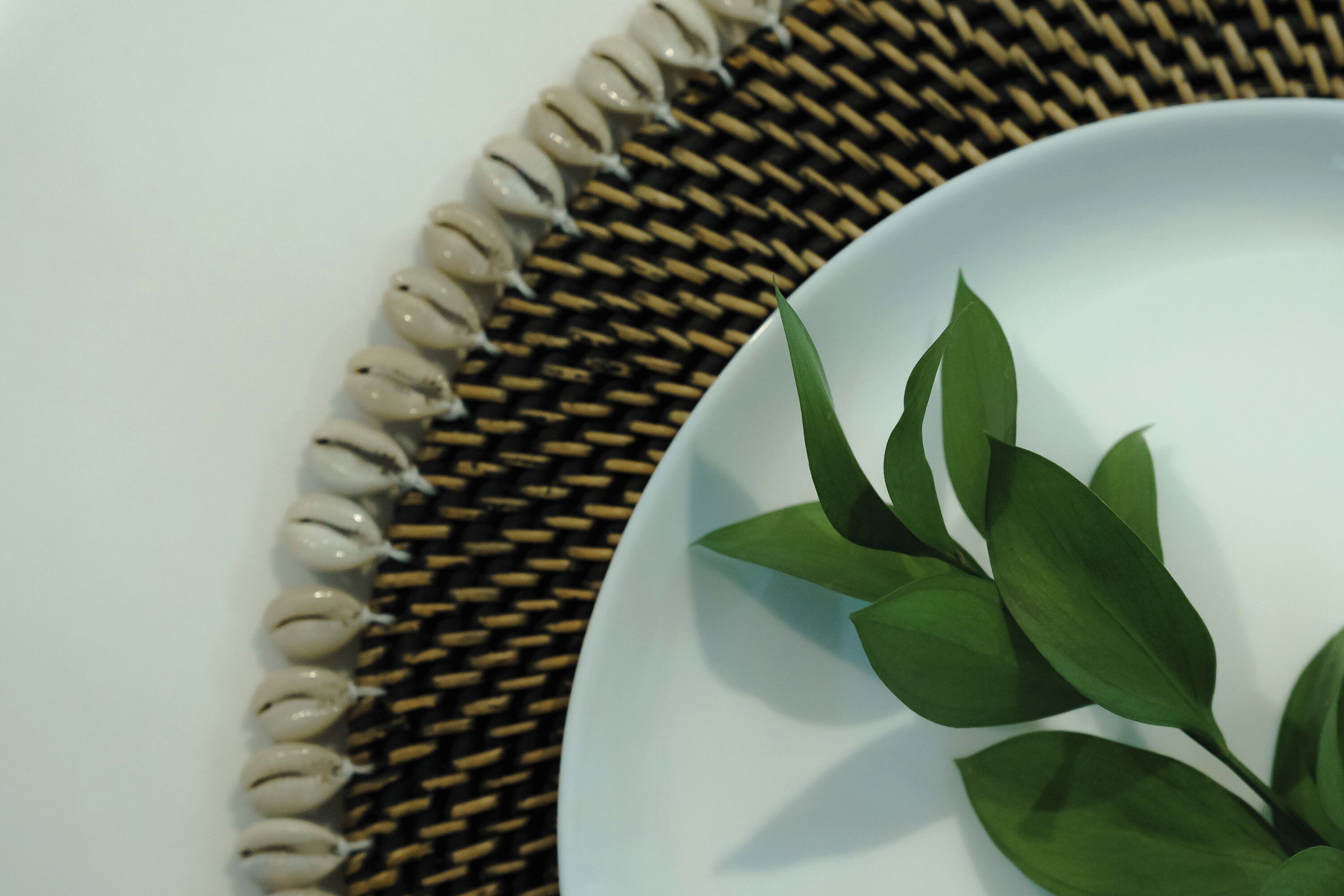 A white plate with green leaves on a woven mat.