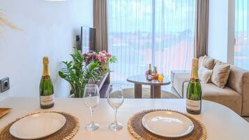 Un comedor moderno con una mesa blanca, dos copas de vino, dos botellas de vino y un jarrón de flores.