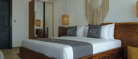 A modern bedroom with a wooden bed, a large mirror, macrame wall hanging, and a woven pendant light.