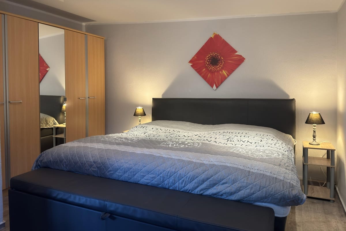 Une chambre à coucher comprenant un lit, des lampes de chevet, une armoire et une décoration florale fixée au mur.