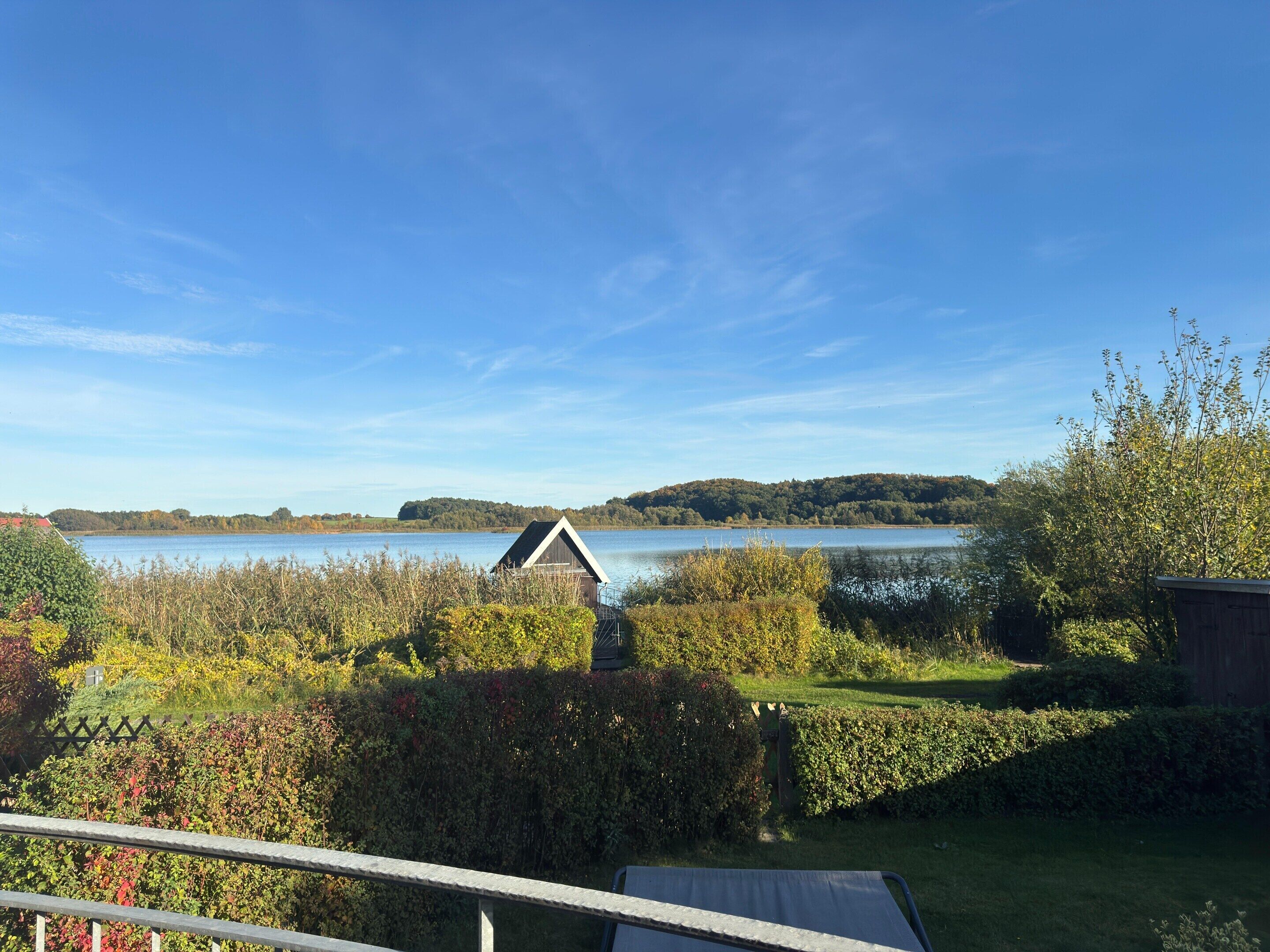 Uitzicht op een meer met een houten chalet, weelderige begroeiing en een helderblauwe lucht.