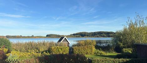 Uitzicht op een meer met een houten chalet, weelderige begroeiing en een helderblauwe lucht.