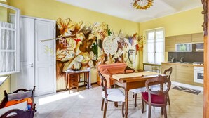 Zona pranzo con tavolo e sedie, un murale al muro e una cucina sullo sfondo.