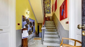 Un corridoio d'albergo con una scala, pareti gialle e opere d'arte.