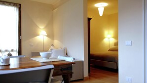 A dining area with a wooden table, chairs, and a bowl. There are two wall-mounted lamps providing light.