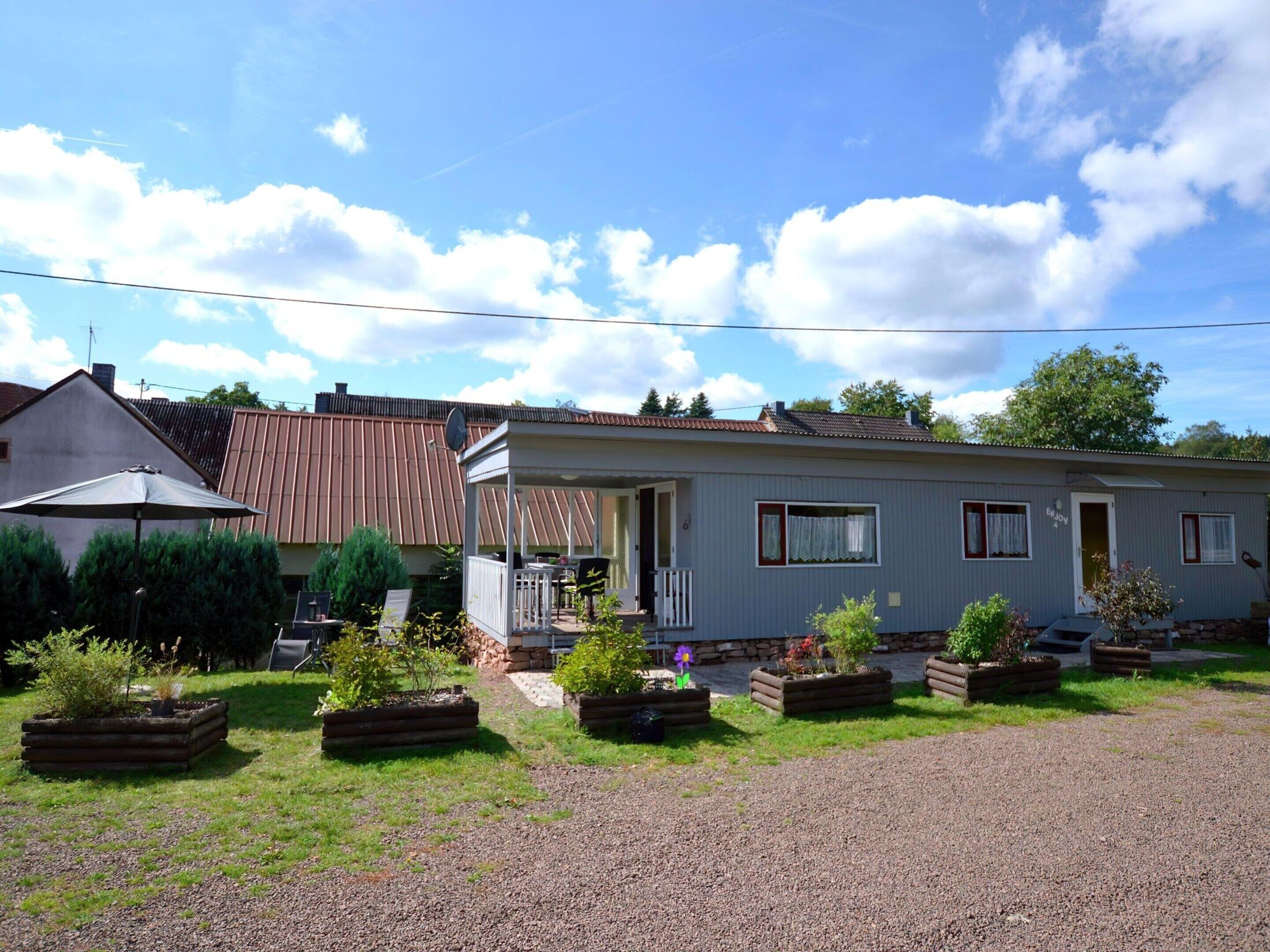 A single-story mobile home with a porch, surrounded by a gravel driveway and small planters.