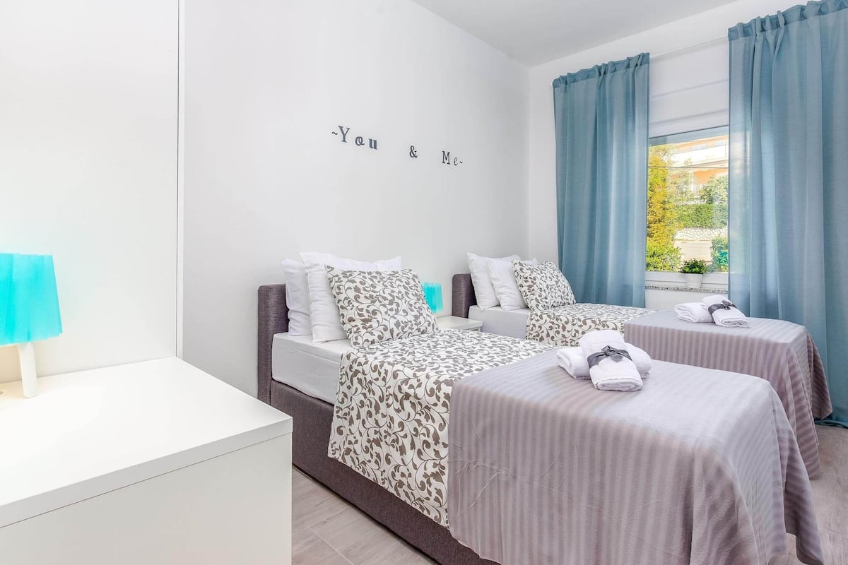 A hotel room with two beds, a small bedside table, and a window with curtains.