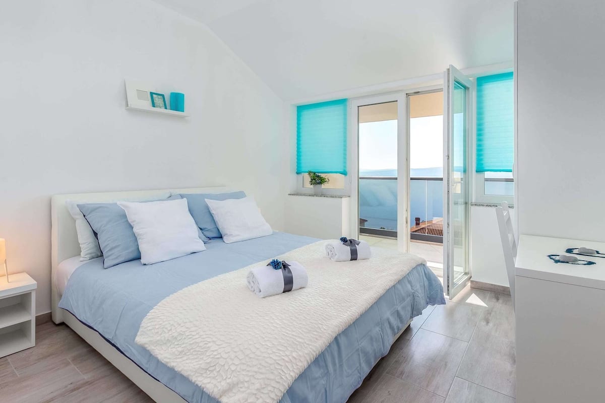 A bedroom with a bed, a nightstand, a desk, and a window with a view.