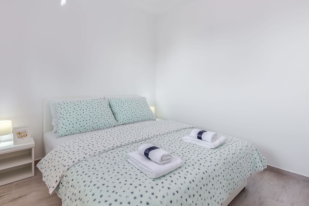 A neatly made bed with a patterned bedspread, pillows, and folded towels.