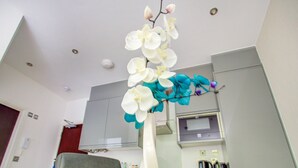 A modern kitchen with white cabinets, a glass dining table, and a vase with white and blue orchids. - Simplistic Apartment in Milton Keynes Near Willen Lake (Milton Keynes)