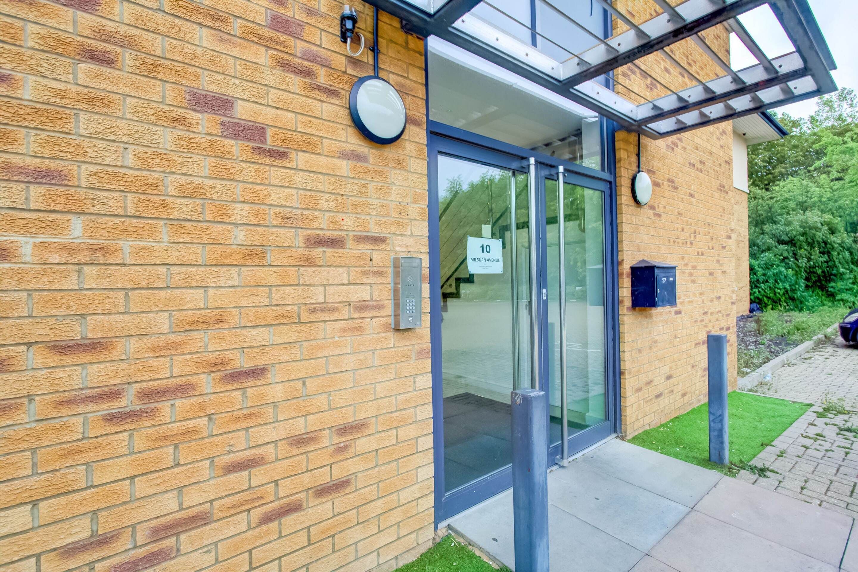 A modern building with a brick facade, glass doors, and a small garden area.