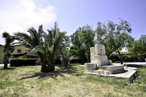Um monumento de pedra numa área gramada, com palmeiras e um edifício ao fundo.