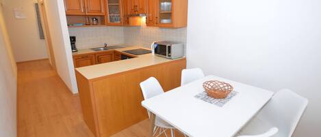 A compact kitchen with wooden cabinets, a microwave, and a dining area with a white table and chairs.