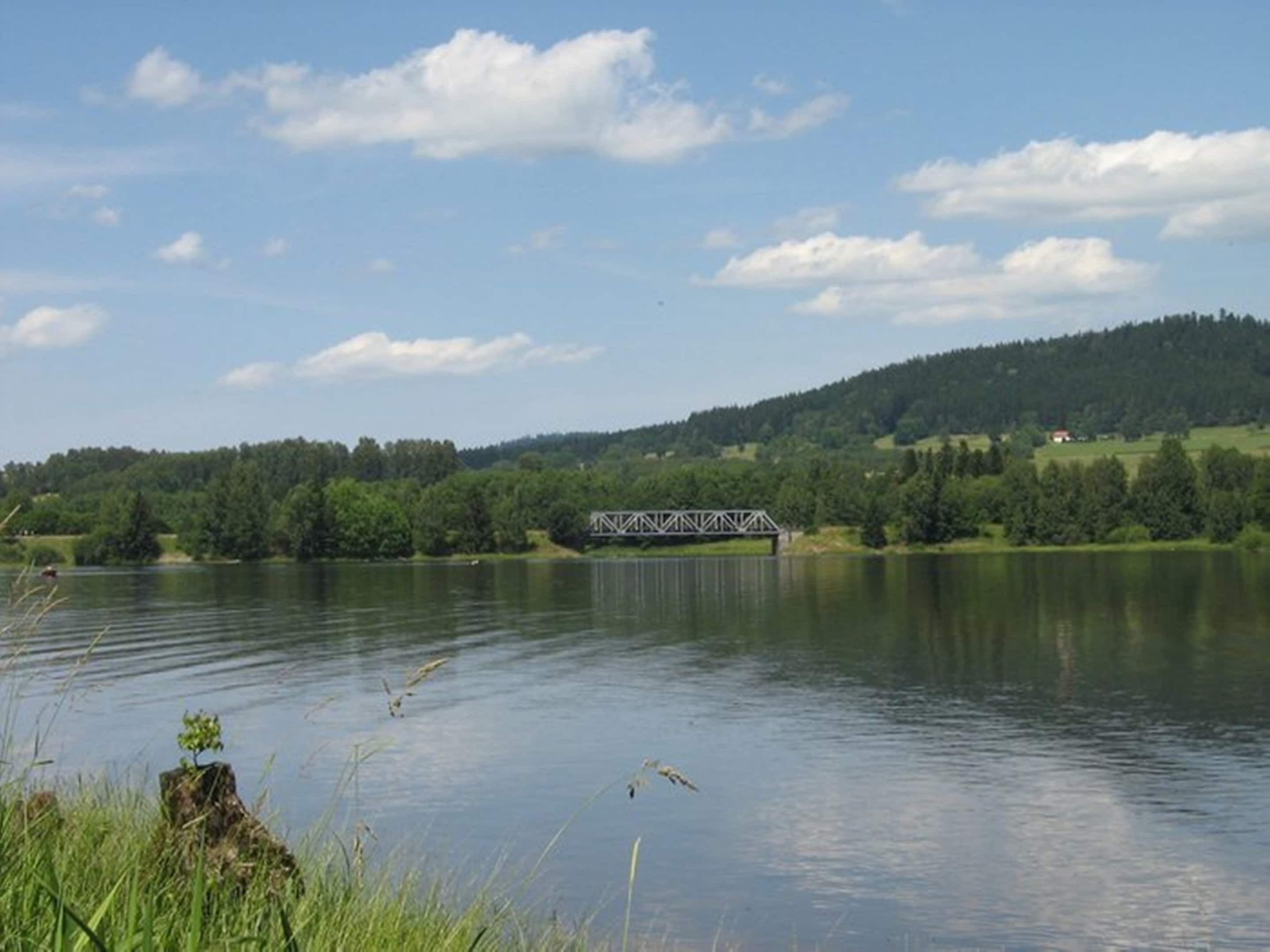 A tranquil lake with a bridge and forested hills in the background.