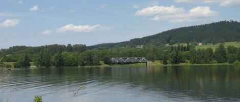 A tranquil lake with a bridge and forested hills in the background.
