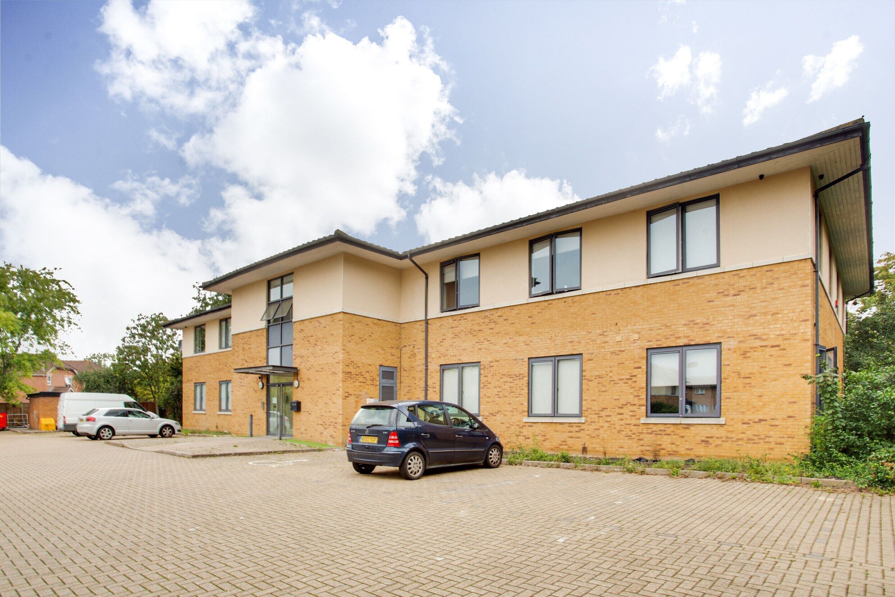 A two-story building with a brick facade, a car parked in front, and a clear sky.