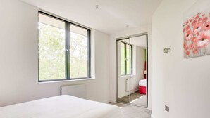 A bedroom with a large window, a bed, a radiator, and a door leading to another room. - Apartment in Milton Keynes Near Canary Karaoke (Milton Keynes)