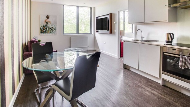 A modern kitchen with a glass dining table, stainless steel appliances, and large windows. - Apartment in Milton Keynes Near Canary Karaoke (Milton Keynes)