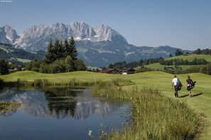 Een golfbaan met een vijver, bomen en bergen op de achtergrond.