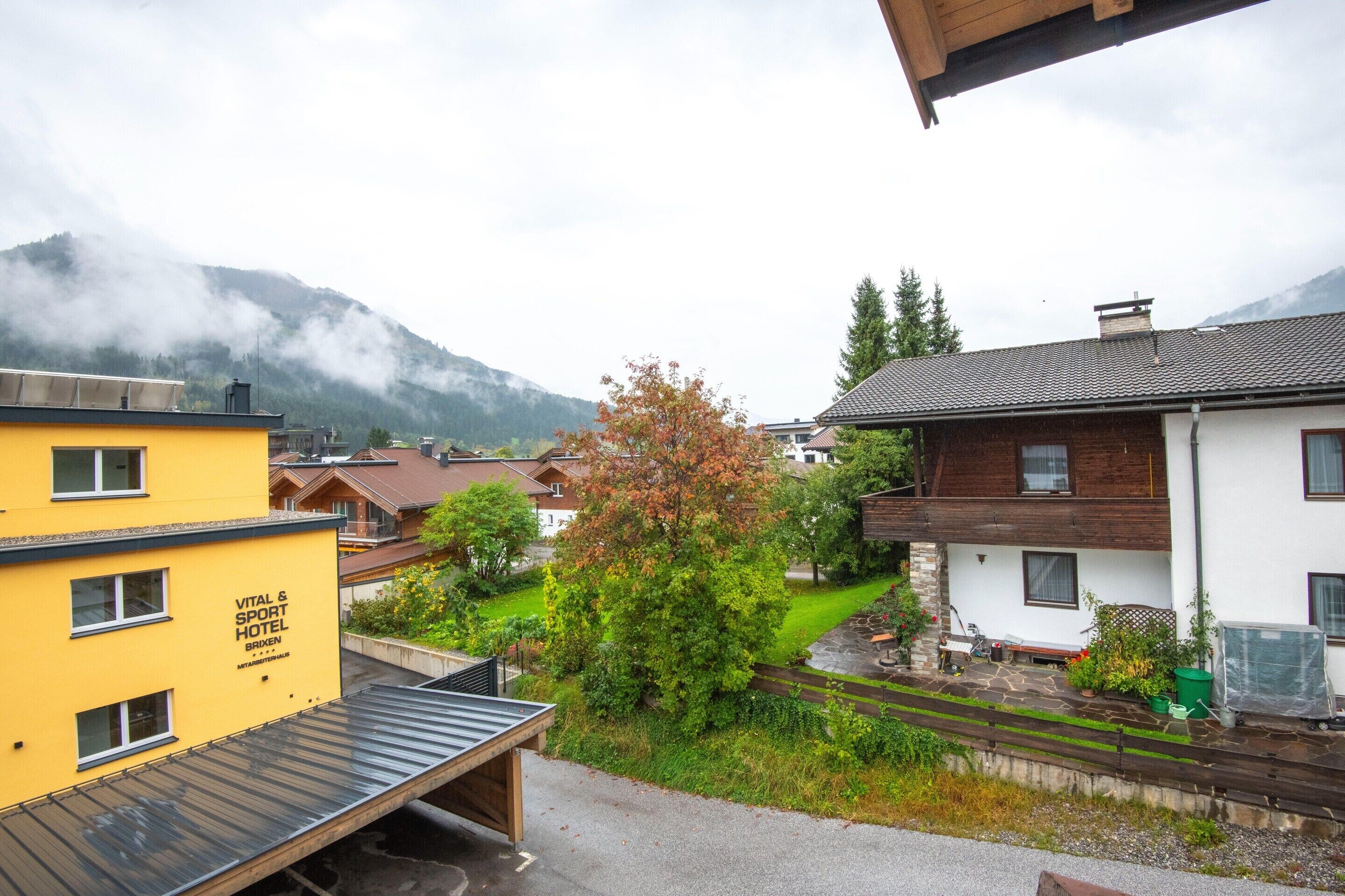A yellow building labeled "VITAL & SPORT HOTEL" with a view of a green garden and a mountain in the background.