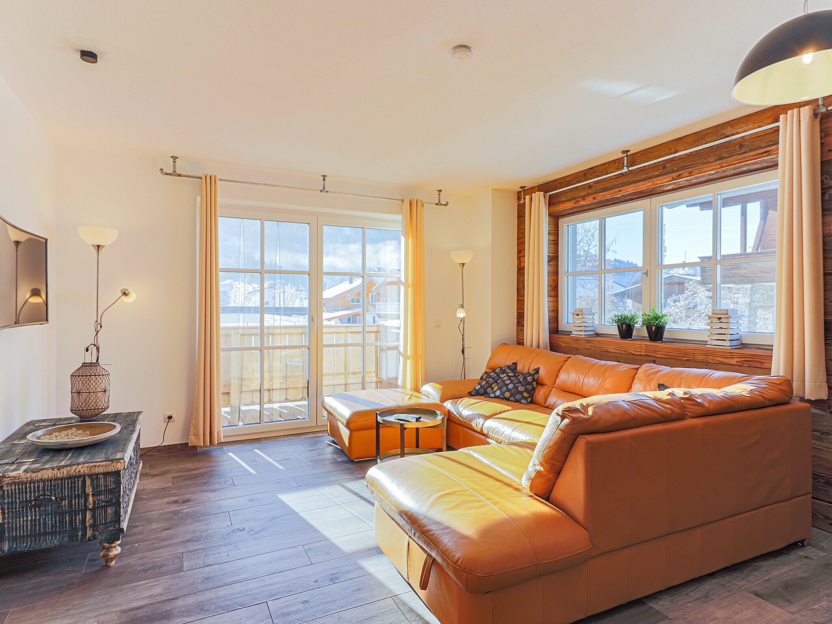 A modern living room with a leather sofa, wooden flooring, and large windows offering a view of the outside.