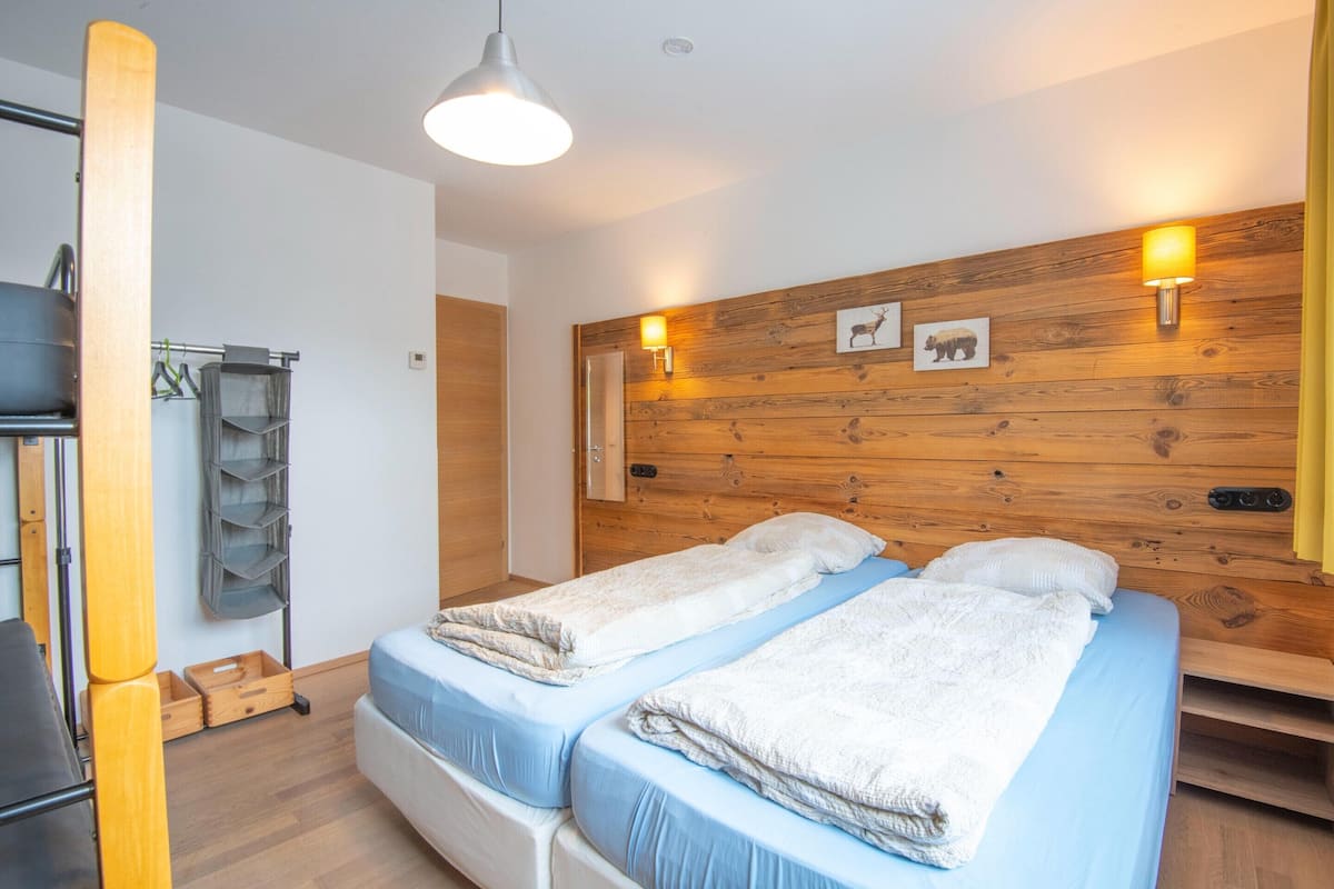 Ein Zimmer mit zwei Betten, einem Holzkopfende, Wandleuchten und einem Holzregal.